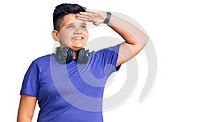 Little boy kid listening to music wearing headphones very happy and smiling looking far away with hand over head