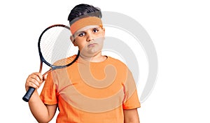 Little boy kid playing tennis holding racket thinking attitude and sober expression looking self confident