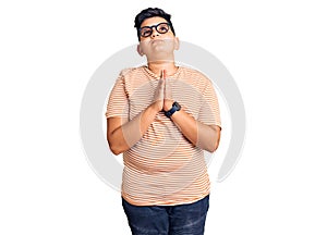 Little boy kid wearing casual clothes and glasses begging and praying with hands together with hope expression on face very