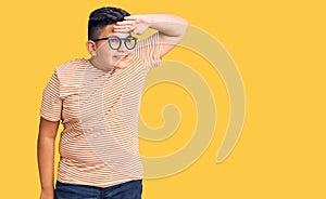 Little boy kid wearing casual clothes and glasses very happy and smiling looking far away with hand over head