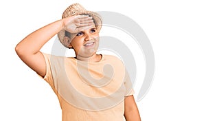 Little boy kid wearing summer hat and hawaiian swimsuit very happy and smiling looking far away with hand over head