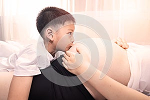 Little boy Kissing the belly of the pregnant mother. Pregnant mother and son are happy.