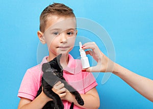 A little boy with a kitten in his arms and his mother`s hand with anti-allergic nosal spray on a blue background photo