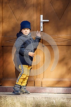 Little boy knocking the brown door in the down city