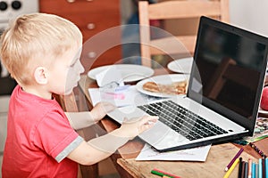 Little boy with laptop on table in home.