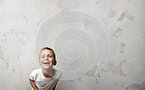 Little boy laughing at the camera. Cocrete wall on