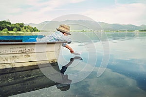 Little boy launch paper ship from old boat on the lake