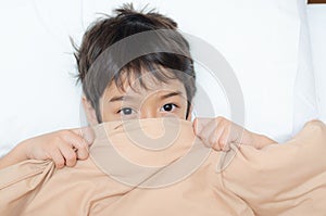 Little boy lay on bed with blanket cover half face