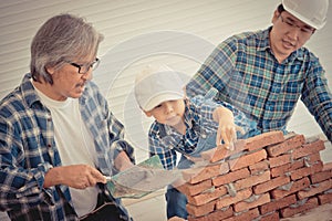 Little boy learning how to build brick wall from his construction Multi generation family