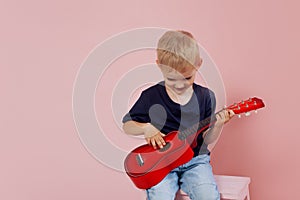 Little boy is learning to play on a small guitar. Study music. Ukulele