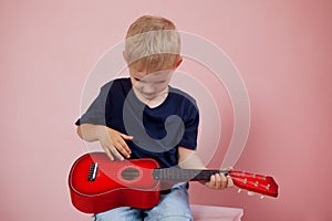Little boy is learning to play on a small guitar. Study music. Ukulele