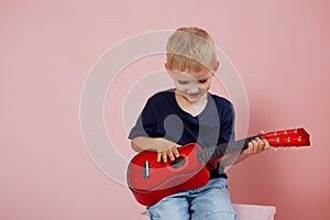 Little boy is learning to play on a small guitar. Study music. Ukulele