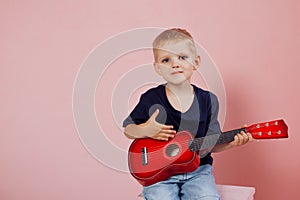 Little boy is learning to play on a small guitar. Study music. Ukulele