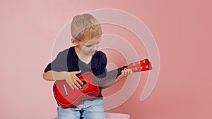 Little boy is learning to play on a small guitar. Study music. Ukulele