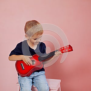 Little boy is learning to play on a small guitar. Study music. Ukulele