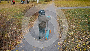 Little boy learning to ride a scooter in a city park. Active leisure and outdoor sport for children.