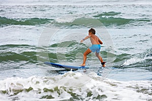 Little boy learning to surf in the stand on board