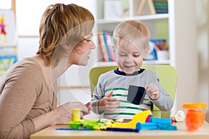 Little boy is learning to use colorful play dough with mother help