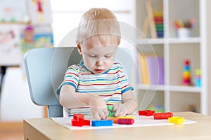 Little boy learning to use colorful play dough in nursery room