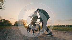 A little boy learns to ride a bicycle under the supervision of his elders