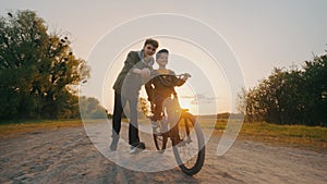 A little boy learns to ride a bicycle under the supervision of his elders