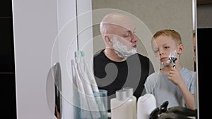 A little boy learns to shave with his dad, he holds a razor and shaves himself.