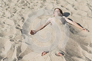 A little boy on the beach buried in the sand