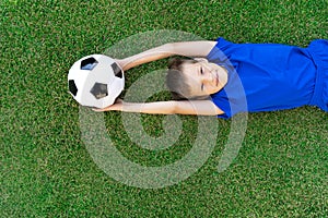 A little boy lies on a green soccer field, a soccer ball, top view