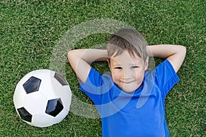 A little boy lies on a green soccer field, a soccer ball, top view
