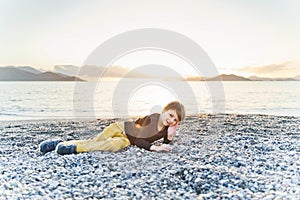 Little boy lies on a pebble beach at sunset
