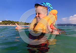 Little boy in life jacket playing with water on the beach