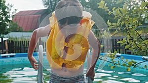 A little boy in life jacket walking out of an inflatable swimming pool