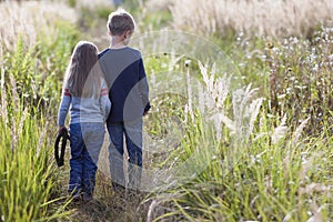 Little boy and little girl standing holding hands looking on horizont. Rear view.