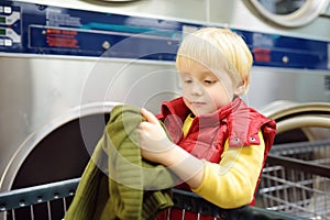 Little boy loads clothes into the drying machine in public laundrette