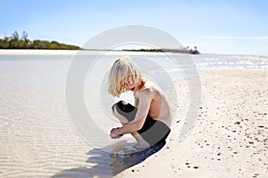 Little Boy with Long Hair Picking Up Seashells on Beach at Ocean