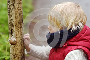 Little boy looking on big snail during hike in forest. Preschooler child explore nature. Developing outdoors activity for kids