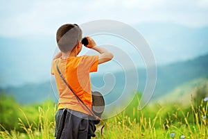 Little boy looking through binoculars outdoor. He is lost.