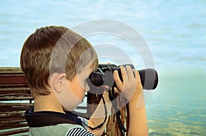 Little boy looking through binoculars at sea. side view, toning