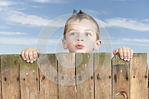 Little boy looking from bove a fence