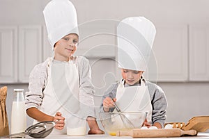 little boy looking at camera and his sister whisking eggs in bowl at table