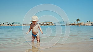 Little boy looking at camera in sunny day. Toddler staying in seawater.
