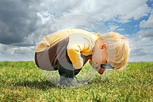 Little Boy Looking at Grass in Nature with Magnifying Glass