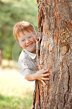 Little boy looking out from behind tree.