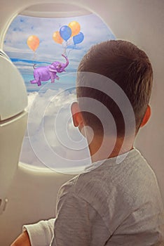 Little boy looking out of window while flying on an airplane.Elephant flying with air balloons with sky and clouds background