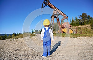 Little boy looking at petroleum pump jack at oil field.