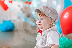 Little boy looking side with mouth covered in white icing and cake in decorated studio backdrop. Birthday cakesmash