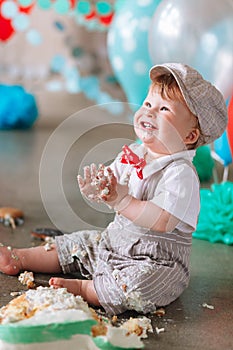 Little boy looking side with mouth covered in white icing and cake in decorated studio backdrop. Birthday cakesmash