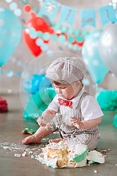 Little boy looking side with mouth covered in white icing and cake in decorated studio backdrop. Birthday cakesmash