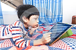 Little boy looking tablet and playing game while lying on the bed at home