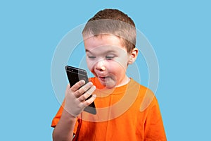 A little boy looks at the phone, and is surprised. Isolated on a blue background